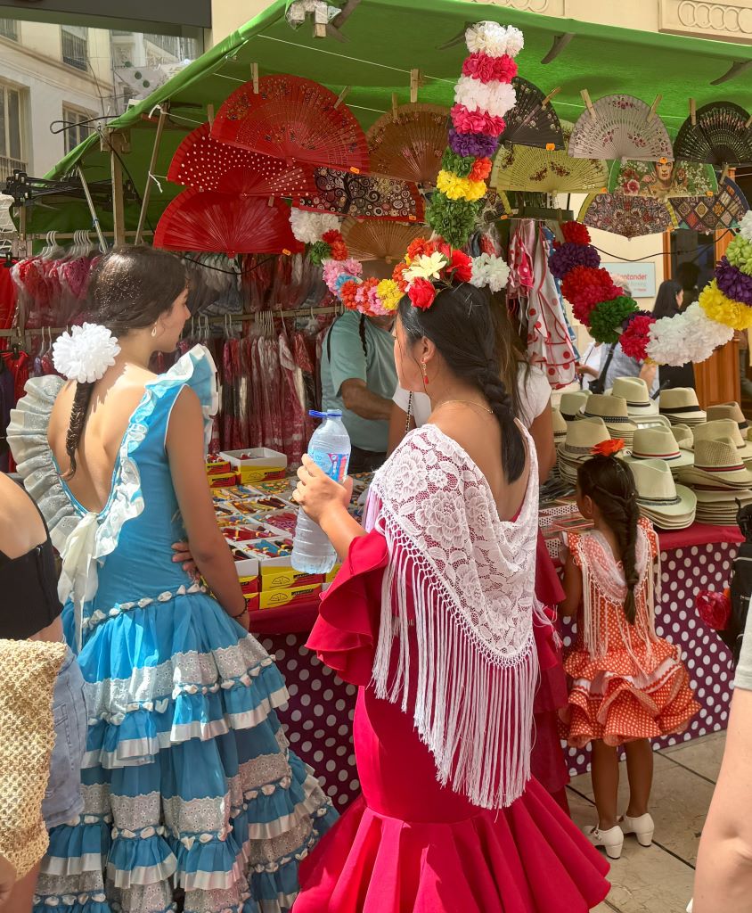 Feria de Malaga (Malaga Fair) 2024. A tent displaying typical products and 3 ladies dressend in Flamenco costumes.